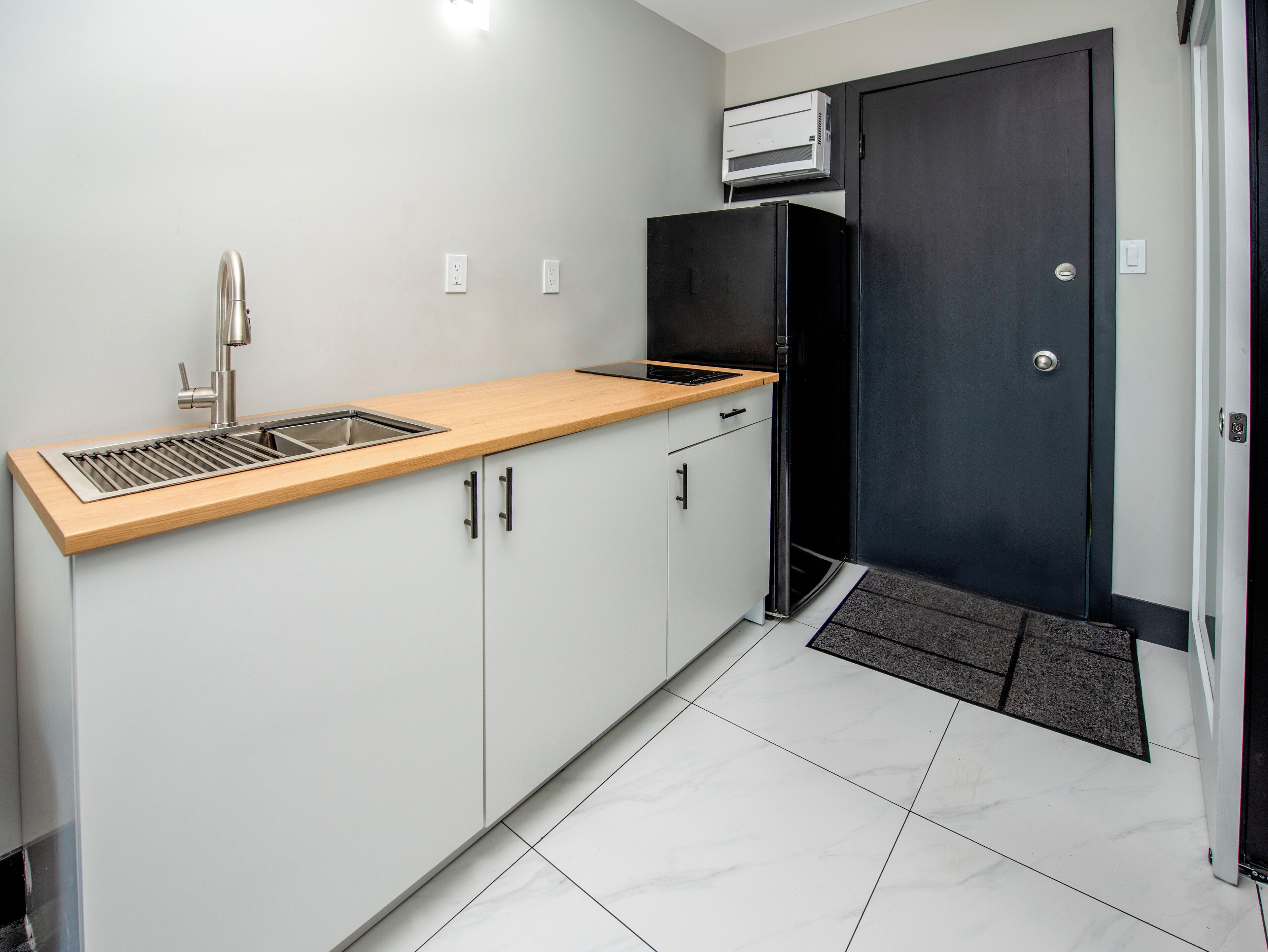 Una cocina moderna con encimera de madera, pileta de acero inoxidable y refrigerador negro.