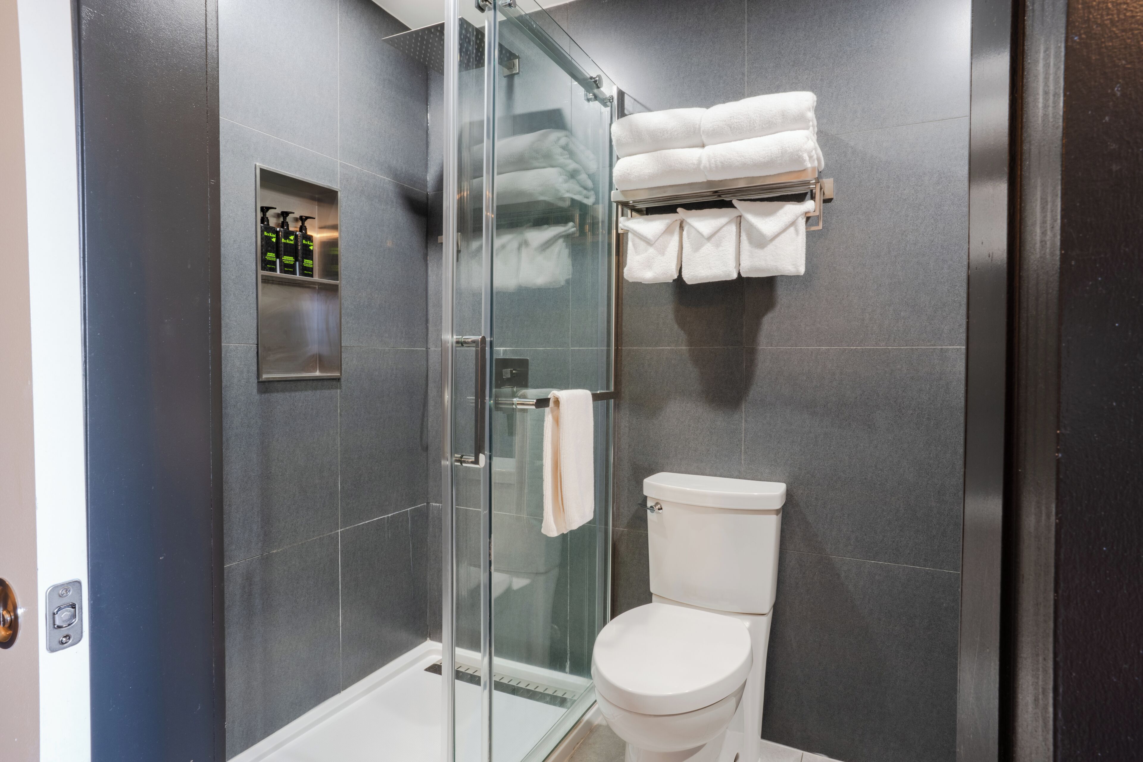 Un baño moderno con ducha de vidrio, inodoro blanco y toallero con toallas dobladas.