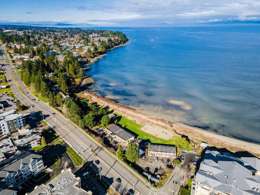 An aerial view of a coastal town with a beach, roads, and residential buildings.