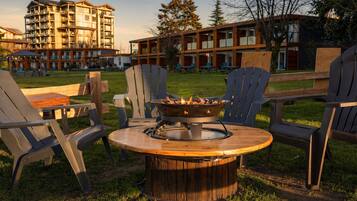 A circular wooden table with a fire pit in the center, surrounded by four Adirondack chairs.
