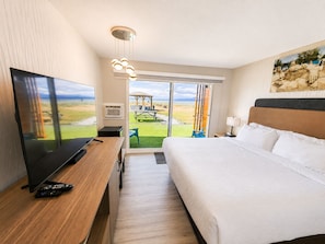 A hotel room with a bed, a TV, a desk, and a view of the beach.