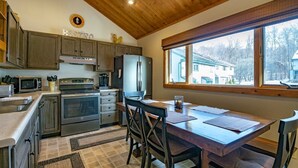 Une cuisine avec des meubles en bois, un réfrigérateur en acier inoxydable, un four à micro-ondes et une cuisinière. On y trouve une table à manger avec des chaises et une fenêtre donnant sur les maisons à l’extérieur.