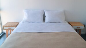 Ein ordentlich bezogenes Bett mit weißen Leinen und einer beigen Decke, an beiden Seiten zwei Nachttische mit Schubladen.