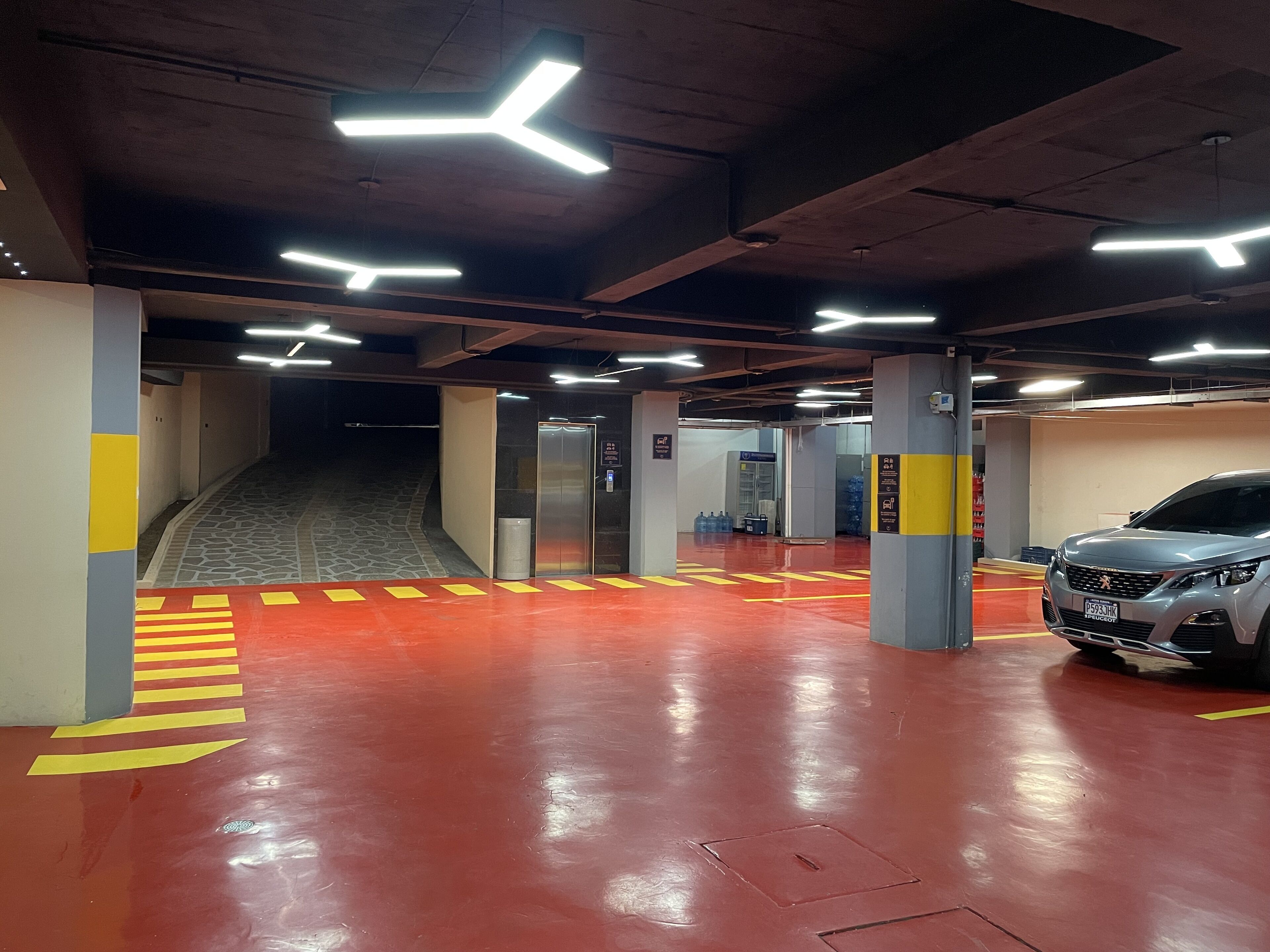 A parking garage with red flooring, yellow directional arrows, and a silver car parked in one of the bays.