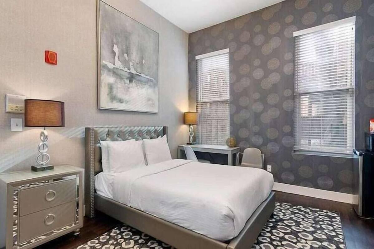 A bedroom with a bed, bedside tables, a desk, and a window with blinds.