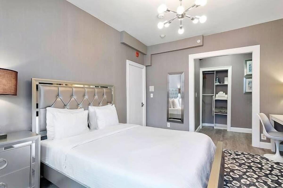 A modern hotel room with a large bed, bedside tables, a desk, and a walk-in closet.