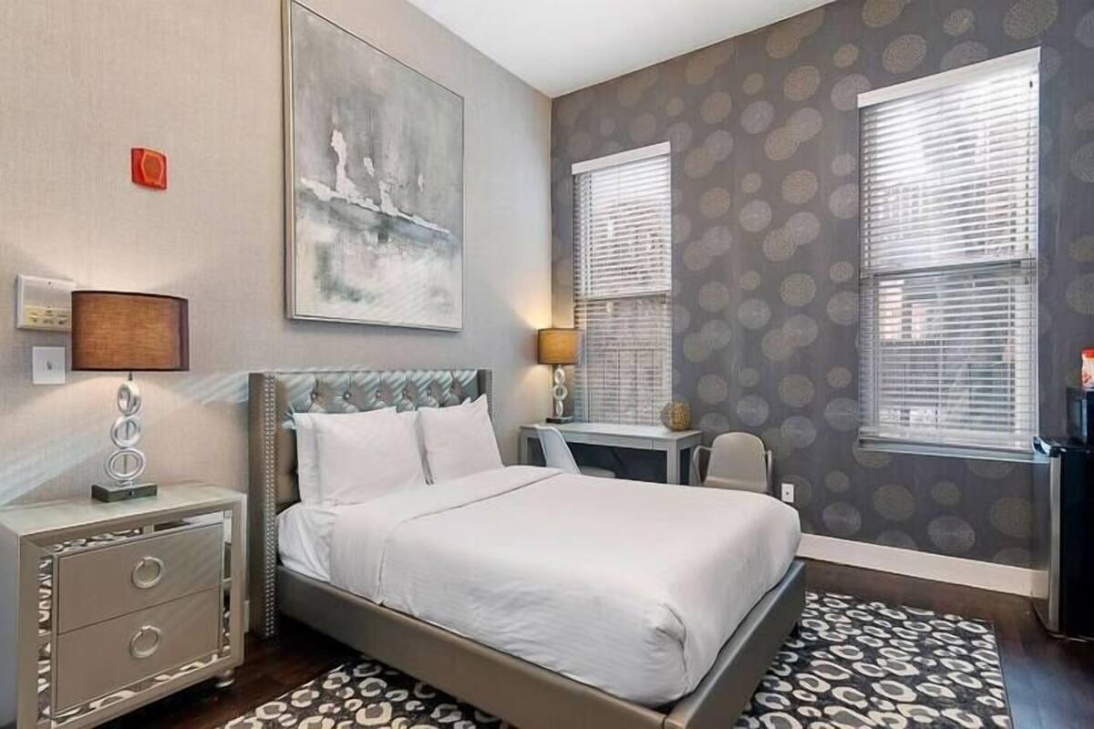 A bedroom with a bed, bedside tables, a desk, and a window with blinds.