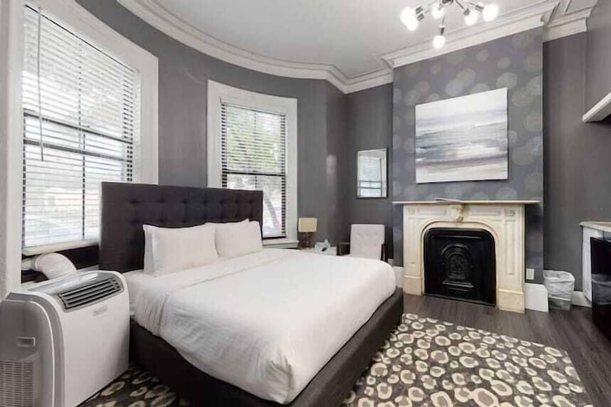 A bedroom with a bed, a fireplace, a radiator, and a large window.