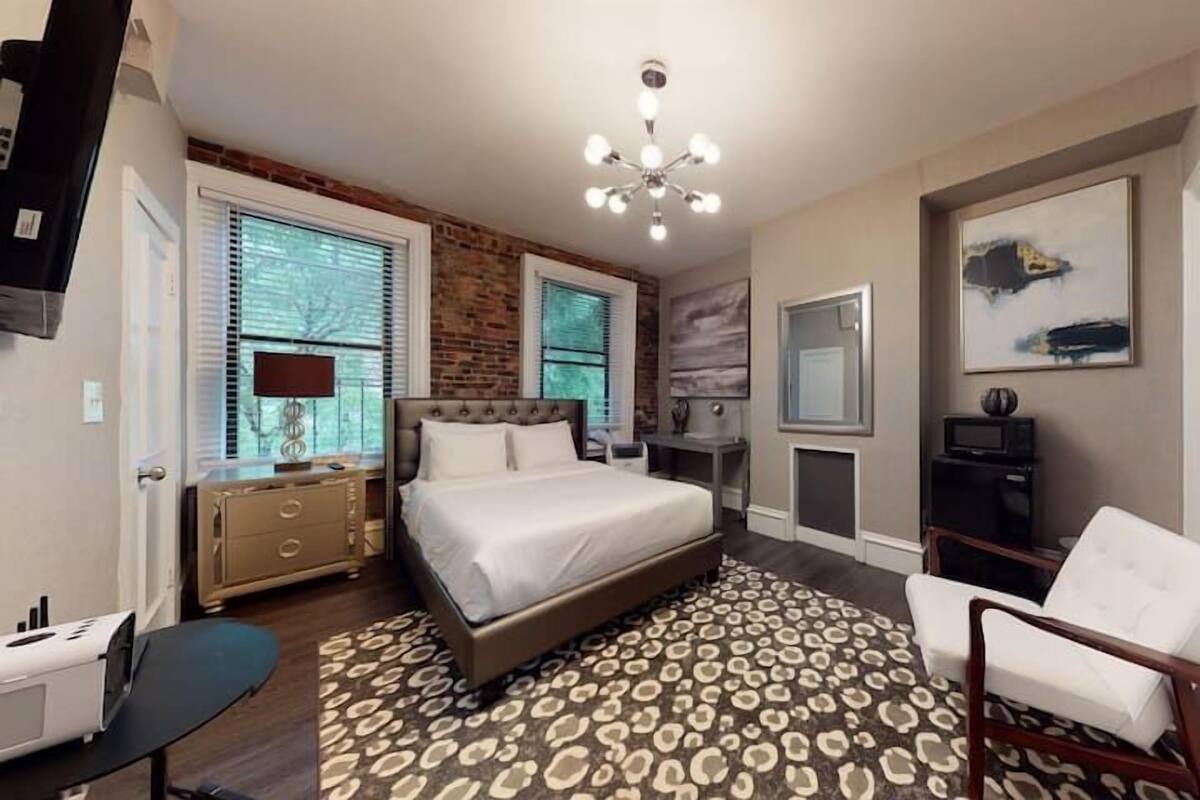 A bedroom with a bed, a desk, a chair, a TV, and a fireplace.