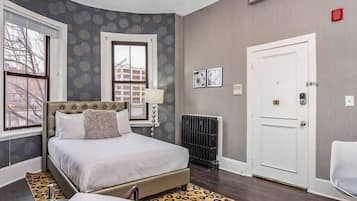 A bedroom with a large bed, a radiator, a white door, and a window with a view of buildings.