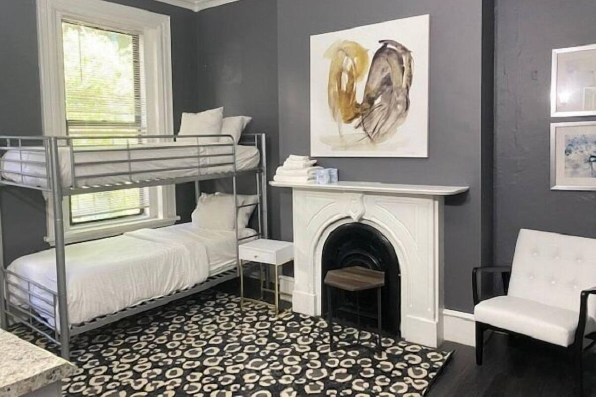 A room with a bunk bed, a fireplace, a leopard print rug, and a white chair.