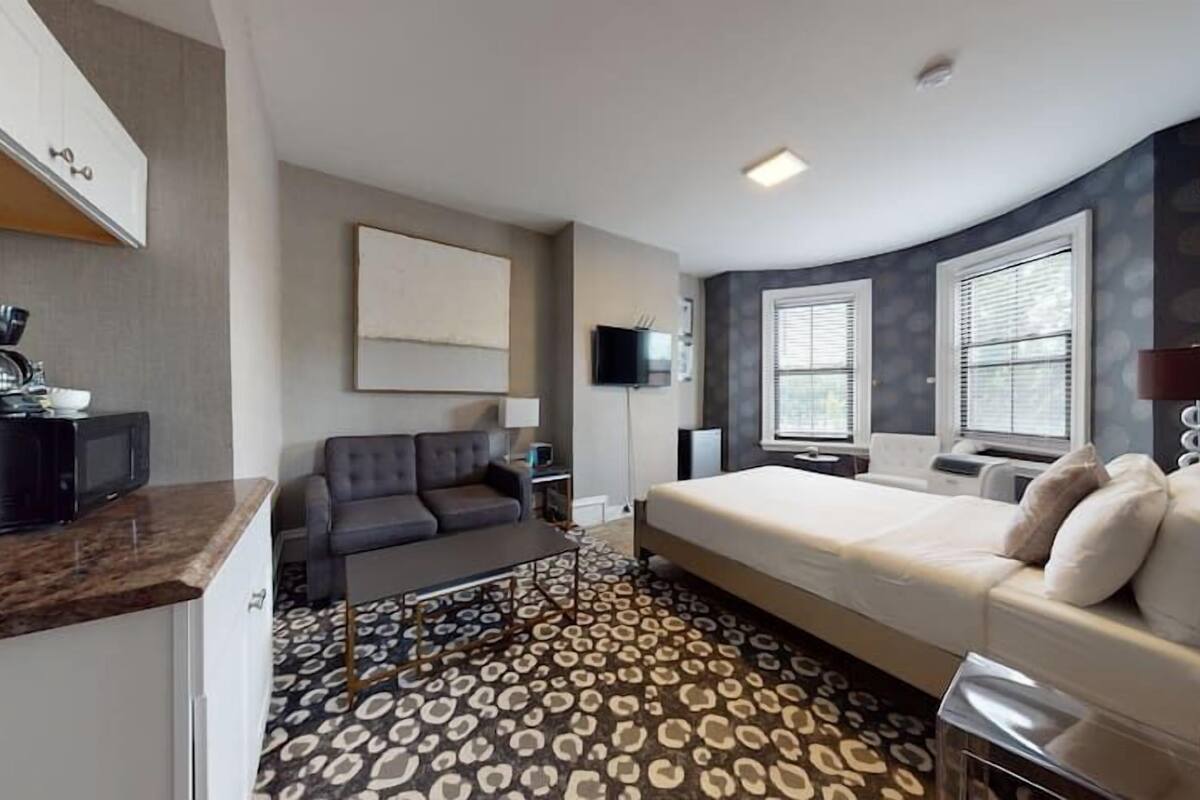 A modern hotel room with a sofa, a bed, a television, and a coffee machine.