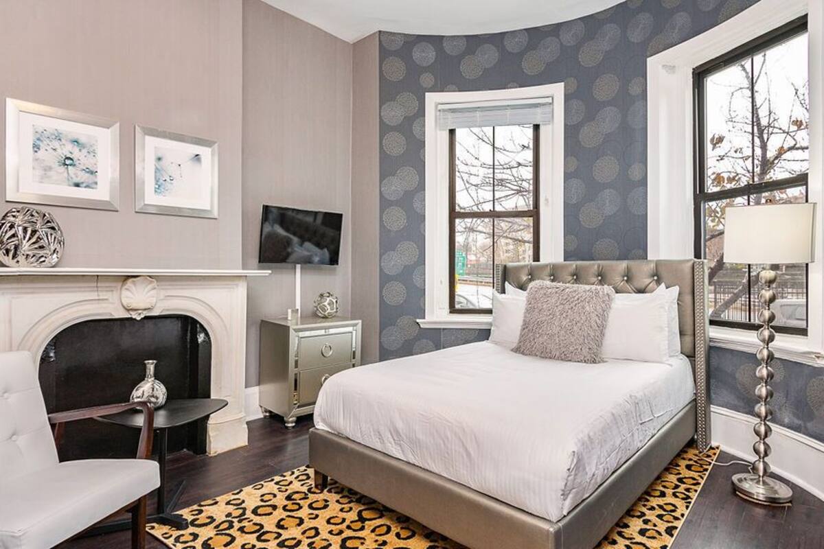 A bedroom with a large bed, a fireplace, a TV, and artwork on the wall.