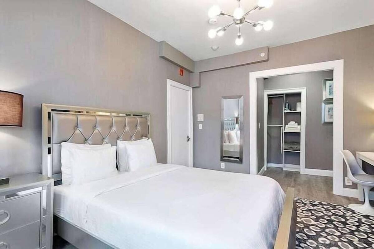 A modern hotel room with a large bed, bedside table, wardrobe, and a desk.