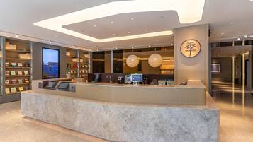 A modern reception desk with a digital screen, a coffee machine, and a cash register. There are shelves with books and a large circular sign with Chinese characters.