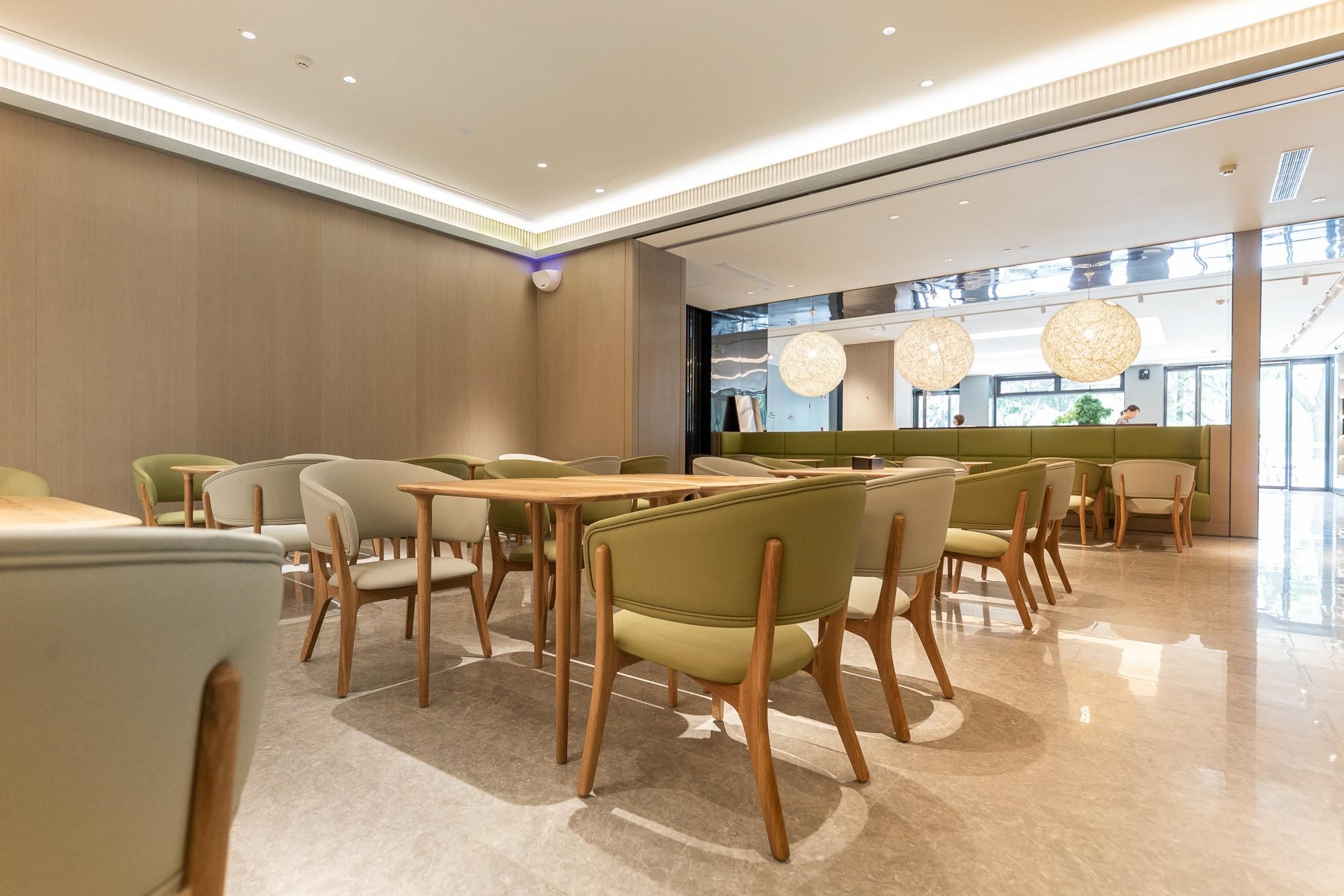 Un restaurant moderne avec des tables et des chaises en bois, un coin salon agrémenté de plantes et de grandes fenêtres laissant entrer la lumière naturelle.