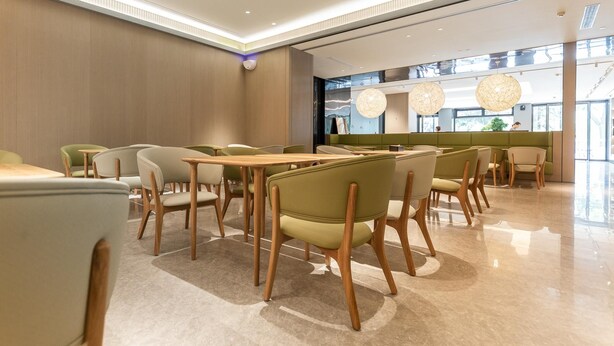 A modern restaurant with wooden tables and chairs, a green booth area, and large windows allowing natural light. - Ji Hotel (Lanzhou)