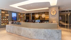 A modern reception desk with a digital screen, a coffee machine, and a cash register. There are shelves with books and a large circular sign with Chinese characters. - Ji Hotel (Lanzhou)