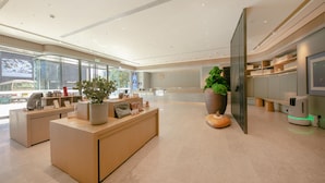 A modern reception area with a reception desk, potted plants, and a large window offering a view of the outside. - JI Hotel (Beijing)