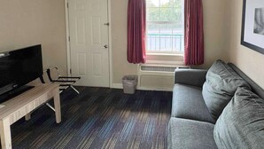 A room with a grey sofa, a TV on a wooden table, a door, and a window with curtains. - Mountain Aire Inn Sevierville/Pigeon Forge (Sevierville)