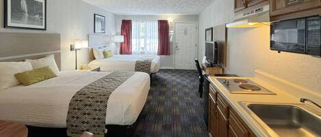 A hotel room with two beds, a kitchenette, a TV, and a window with curtains.