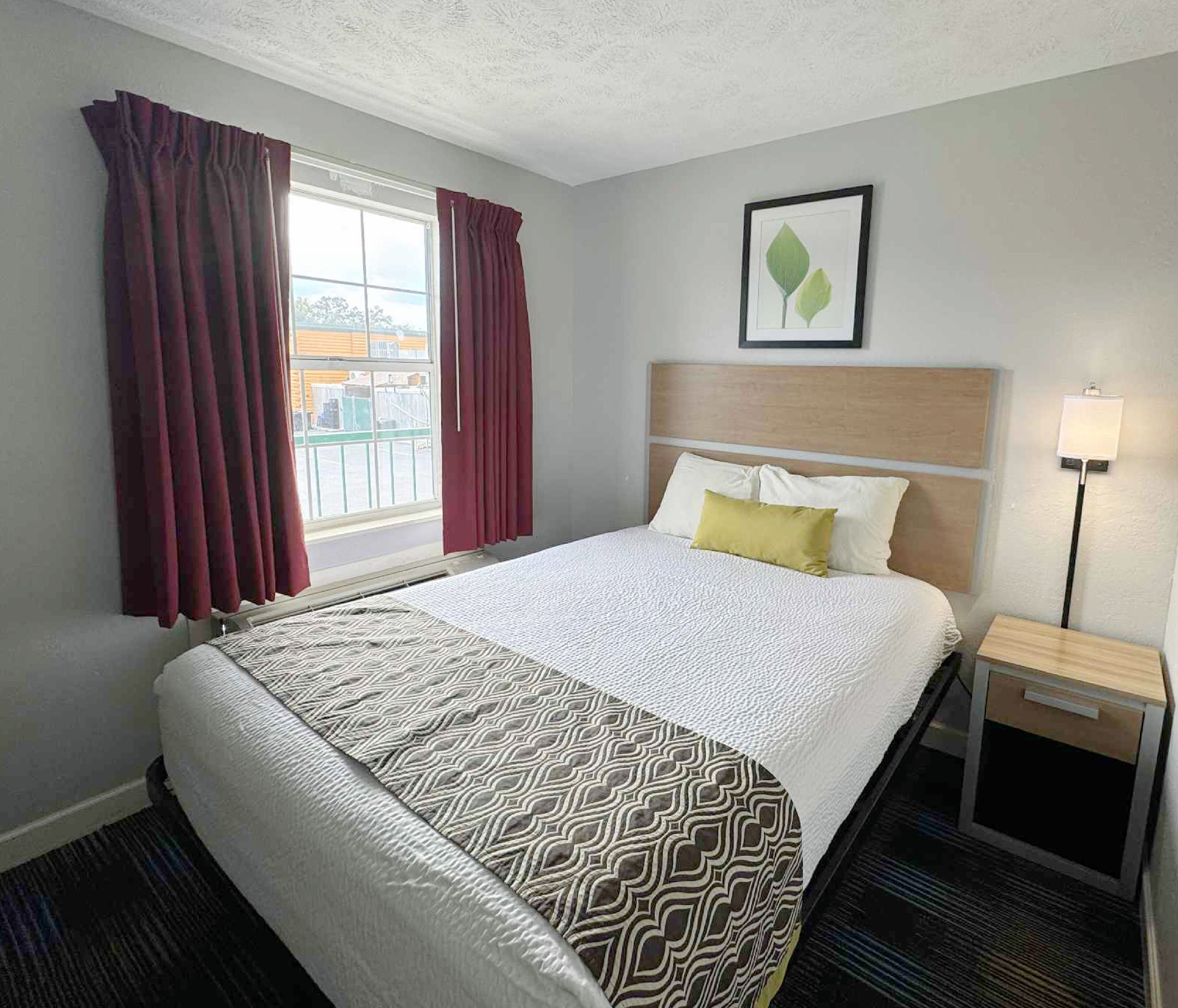 A hotel room with a large bed, a headboard, a bedside table with a lamp, and a window with curtains.