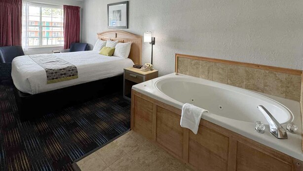 A hotel room with a large bed, a separate sitting area, a bathroom with a bathtub, and a window with curtains. - Mountain Aire Inn Sevierville/Pigeon Forge (Sevierville)
