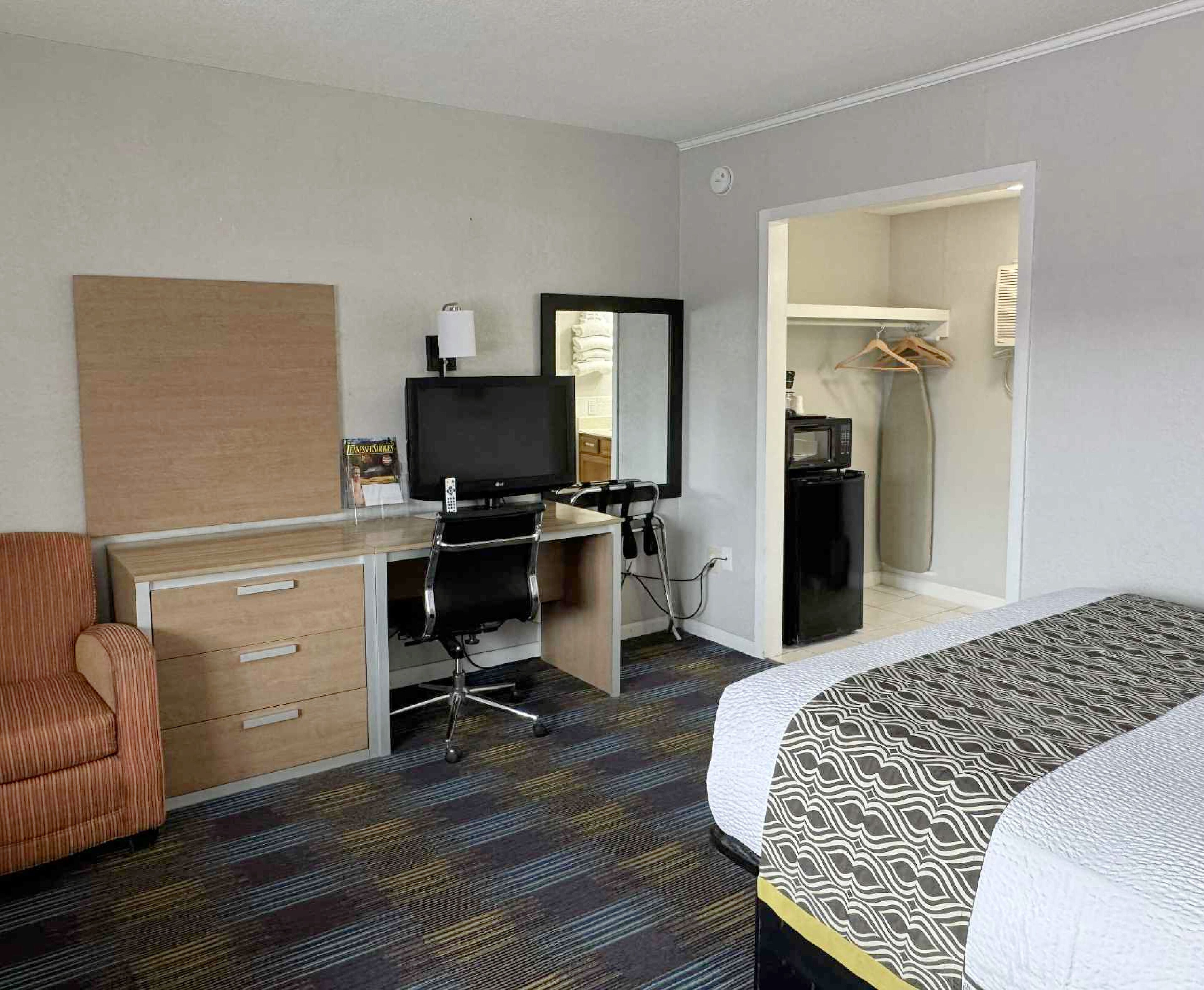 A hotel room with a bed, a desk with a computer, a chair, a television, and a microwave.