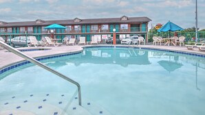 A swimming pool with lounge chairs and umbrellas, surrounded by a building with multiple windows and a brick facade. - Mountain Aire Inn Sevierville/Pigeon Forge (Sevierville)