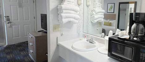A hotel bathroom with a white sink, a mirror, a hairdryer, and a coffee maker.