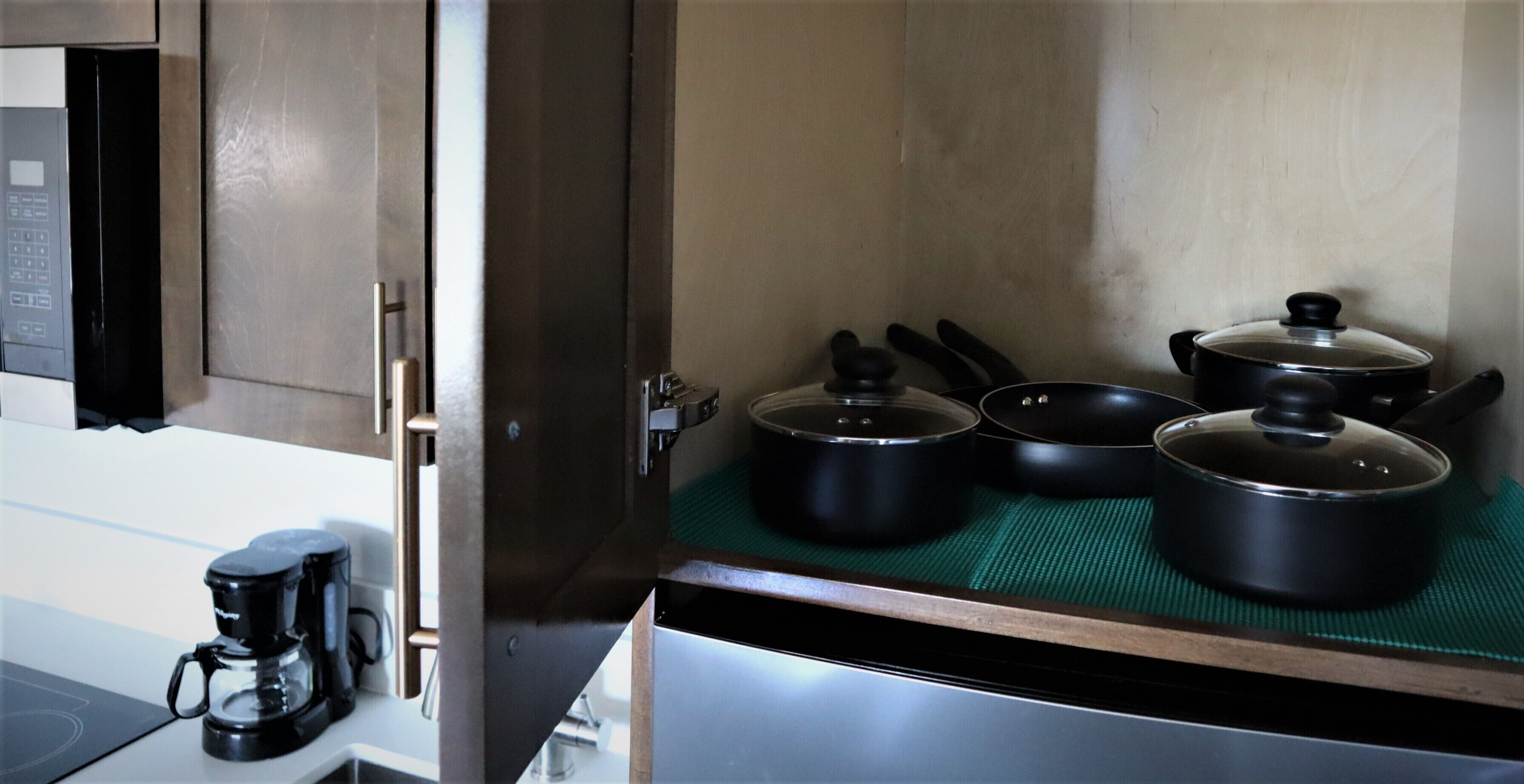 A kitchen with a microwave, coffee maker, and pots on a green mat.