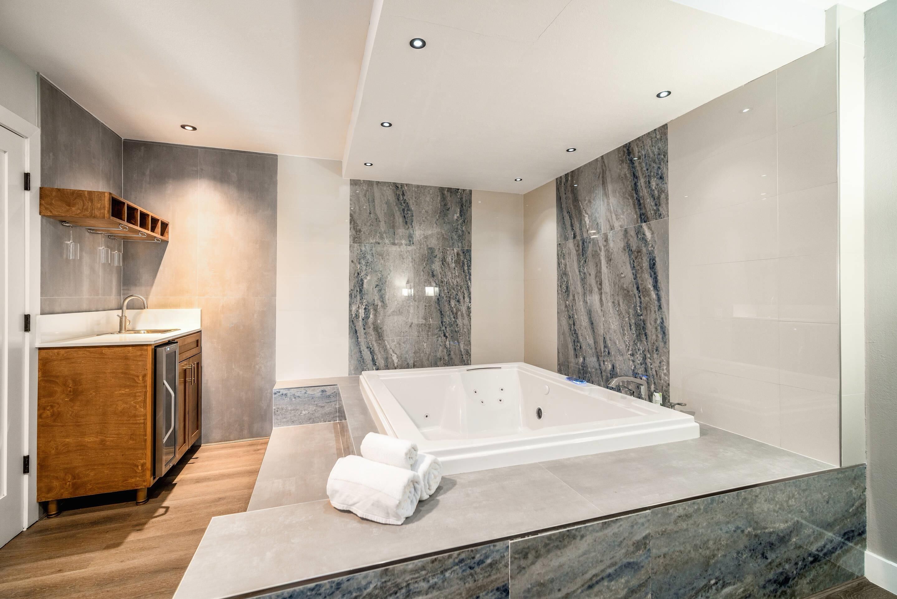A modern bathroom with a large bathtub, wooden cabinetry, and marble walls.