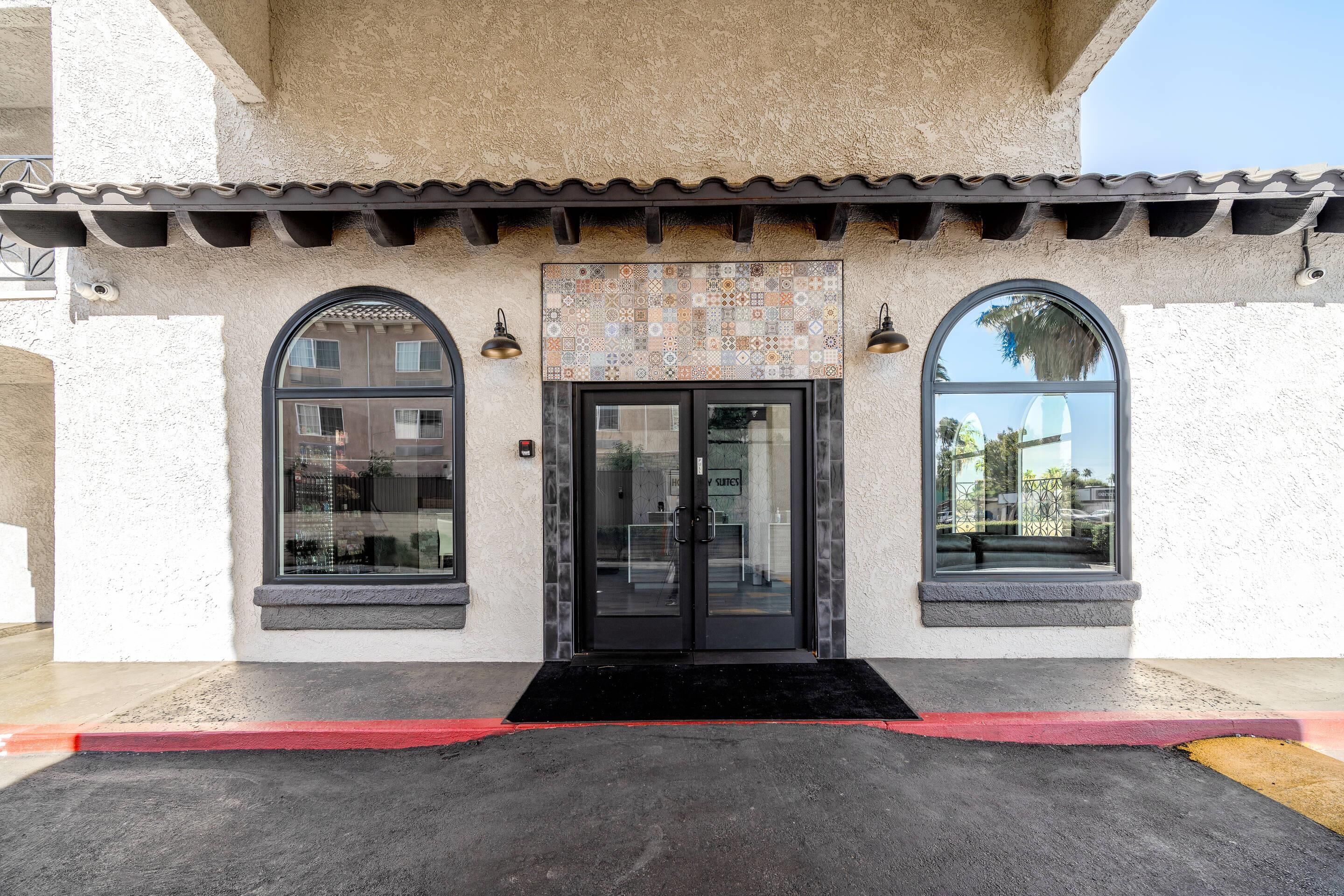 A hotel entrance with a tiled facade, a black door, and two arched windows.