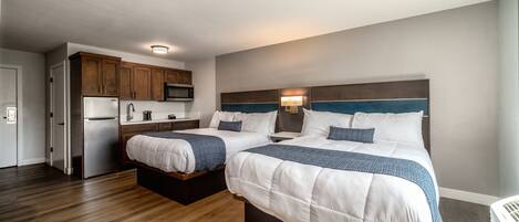 Habitación de hotel con dos camas, una kitchenette y piso de madera.