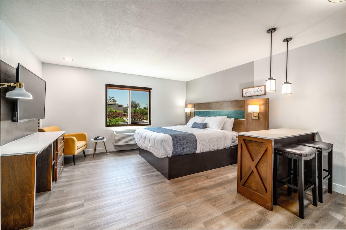 A modern hotel room with a bed, a desk, a chair, and a small table.