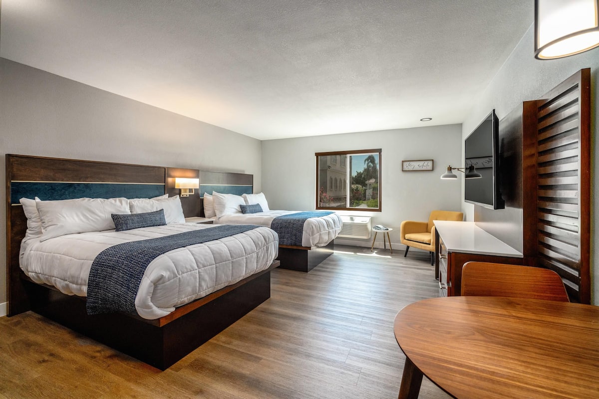 A hotel room with two beds, a desk, a chair, a TV, and a window with a view.