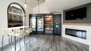 A modern bar area with a long counter, white bar stools, a large arched window, and a fireplace. - MainStay Suites Moreno Valley Near March Air Reserve Base (Moreno Valley)