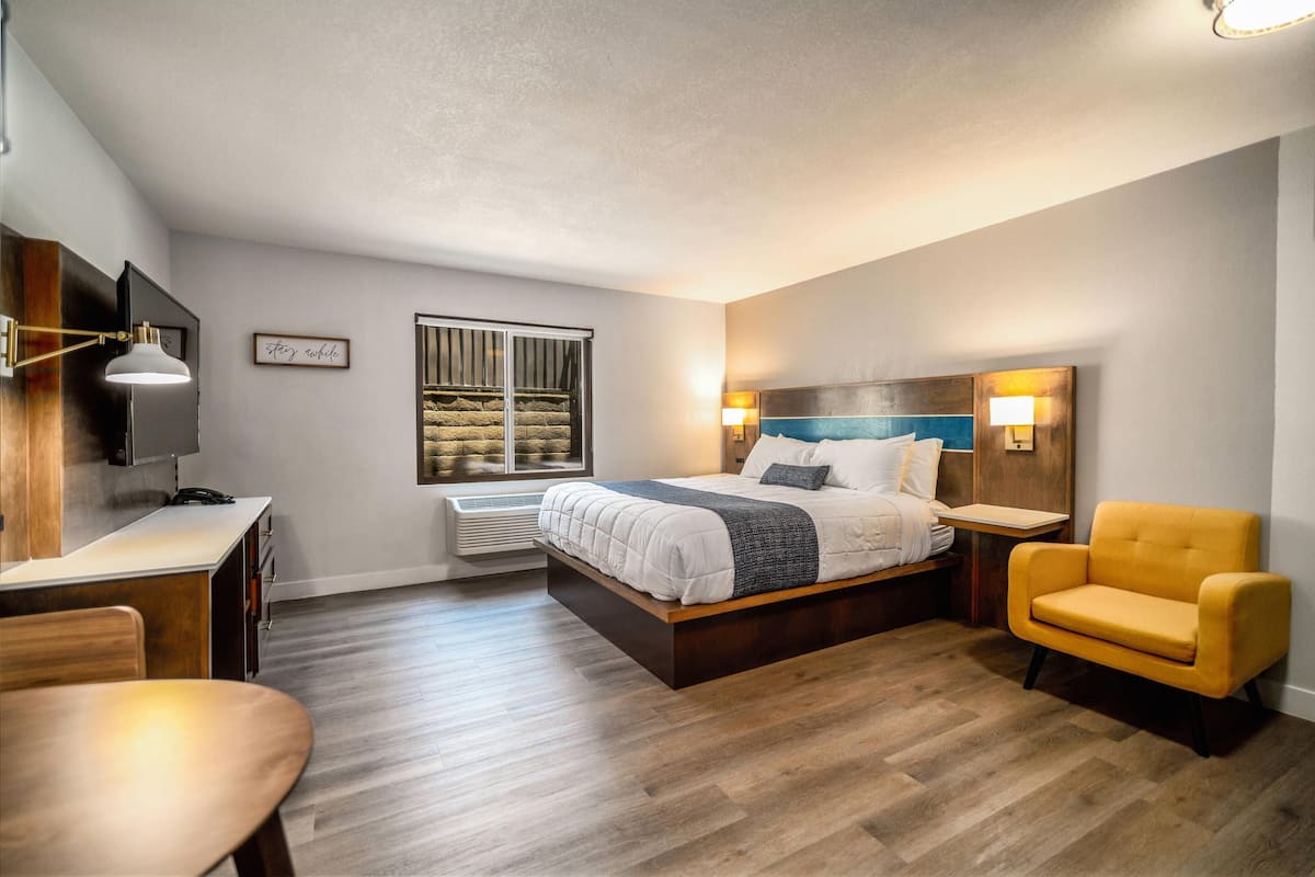 A modern bedroom with a bed, bedside tables, a desk, a chair, and a window.
