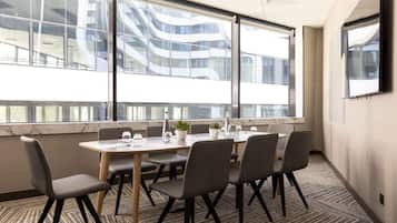Uma sala de conferências com uma mesa grande, seis cadeiras e vista para um edifício moderno com janelas de vidro.