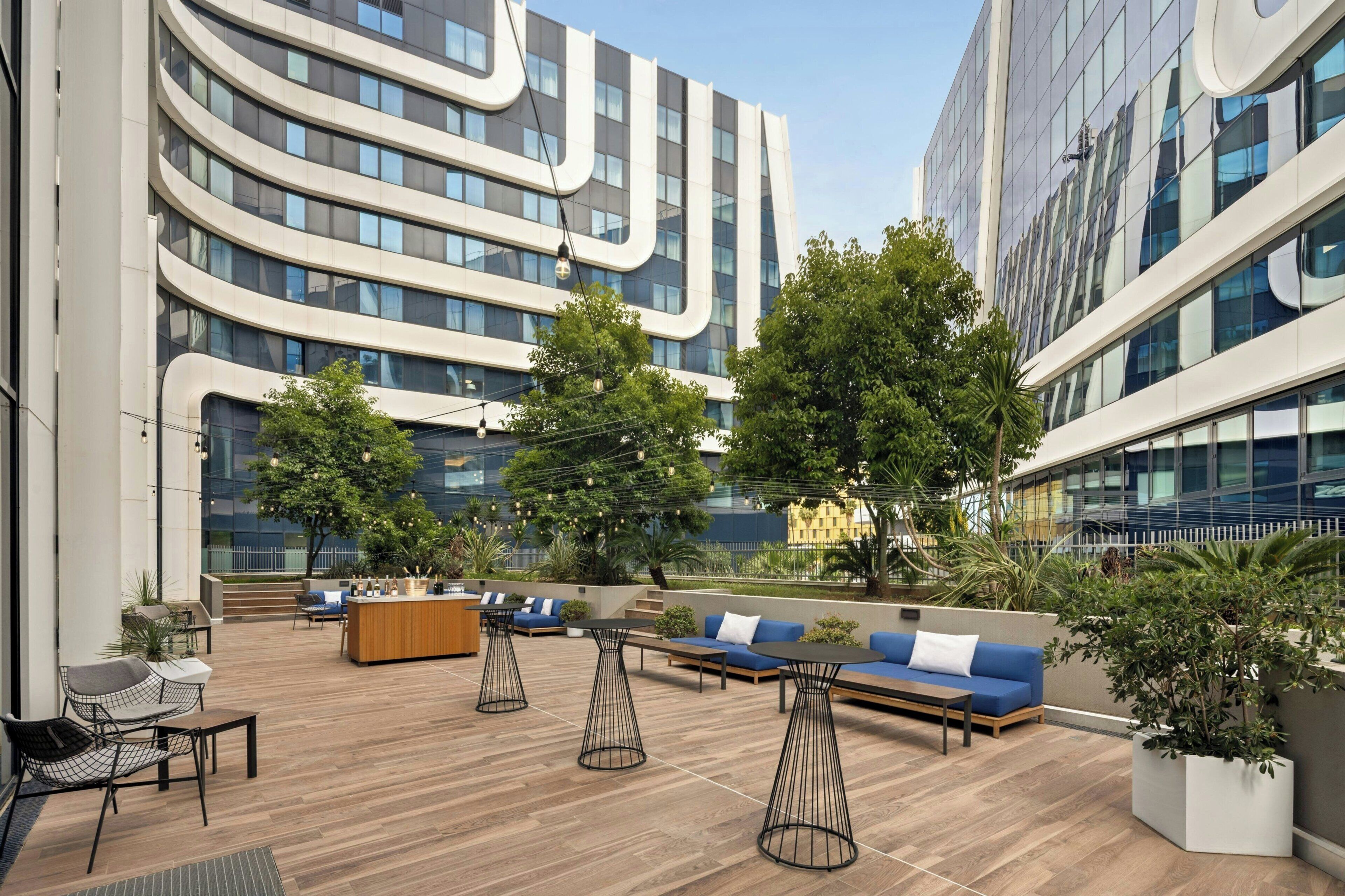 A rooftop terrace with seating areas, a bar, and a view of modern buildings.