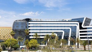 A modern Sheraton hotel with a curved glass facade, palm trees, and a clear blue sky.