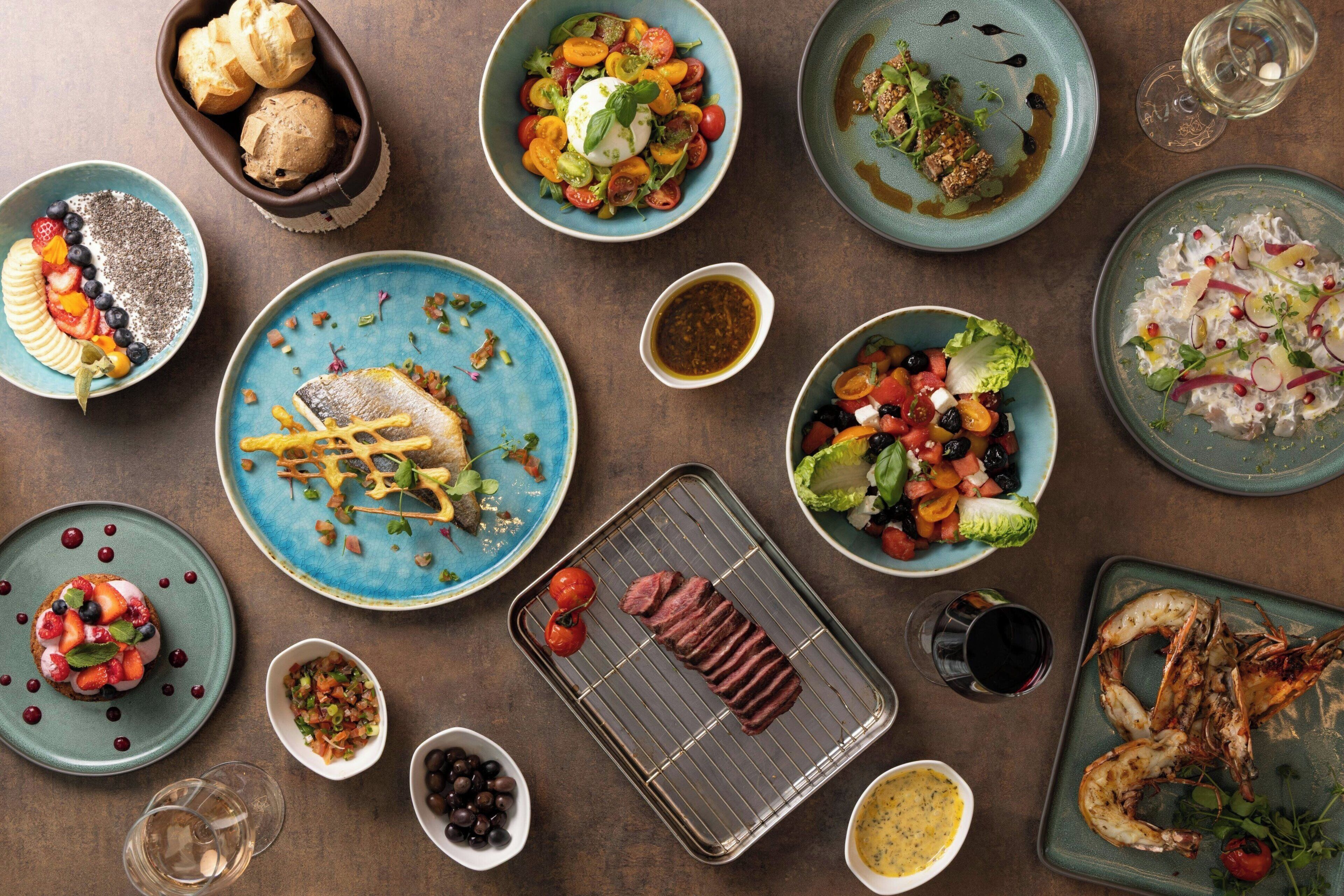 A variety of dishes on a table, including seafood, salads, and a grilled steak.