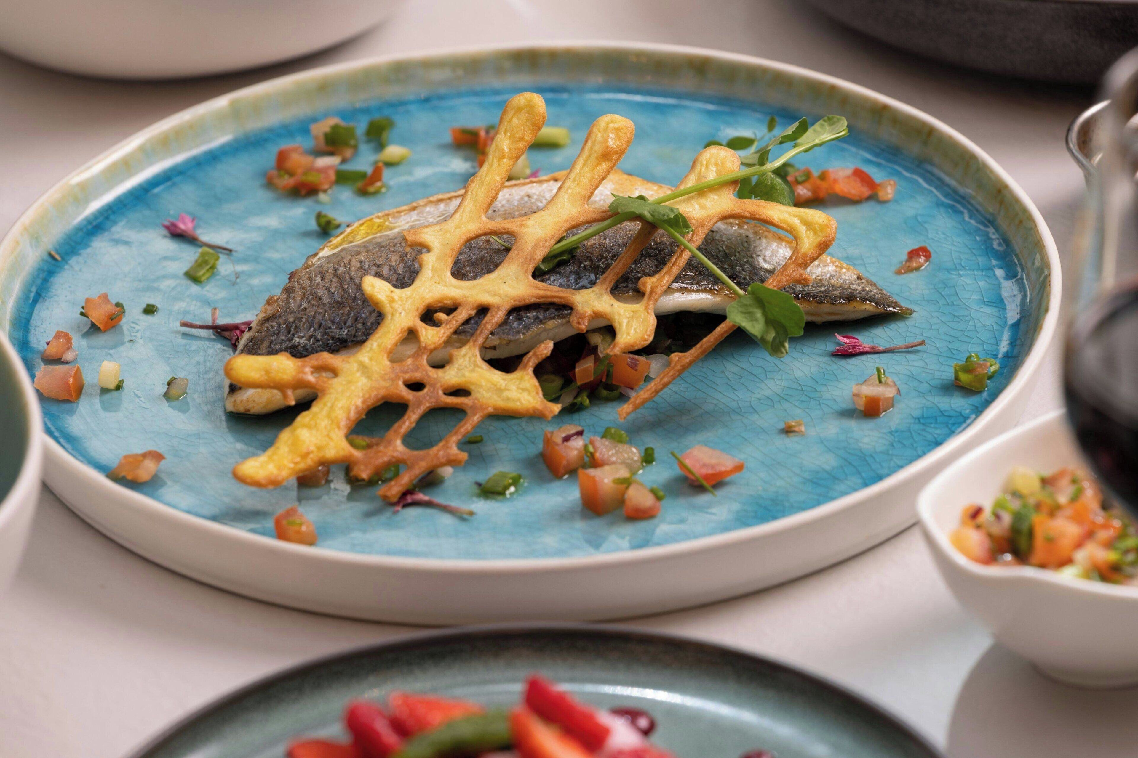 A plate with a fish, vegetables, and a decorative element.