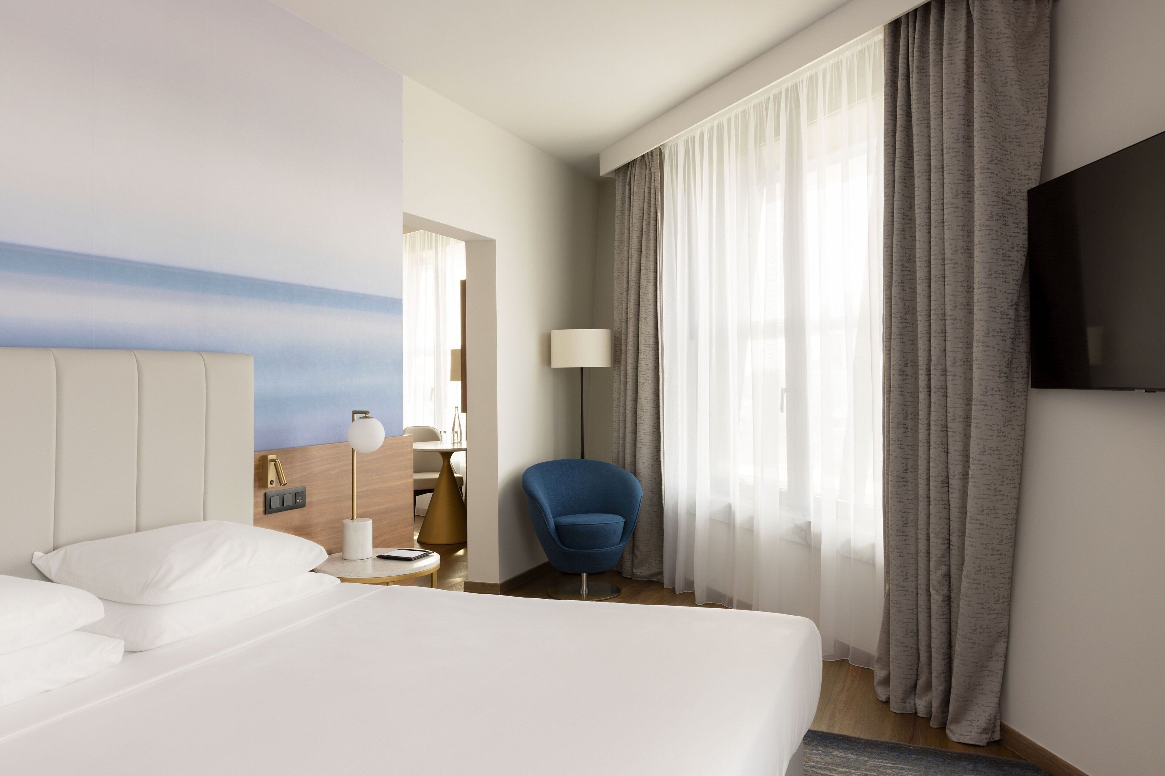 Une chambre d’hôtel avec un grand lit, un bureau avec une lampe, une chaise et un téléviseur fixé au mur.