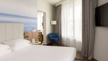 Une chambre d’hôtel avec un grand lit, un bureau avec une lampe, une chaise et un téléviseur fixé au mur.