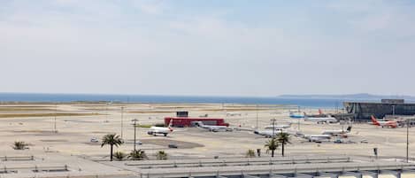 An airport terminal with multiple gates, a covered waiting area, and a clear view of the tarmac with parked aircraft.