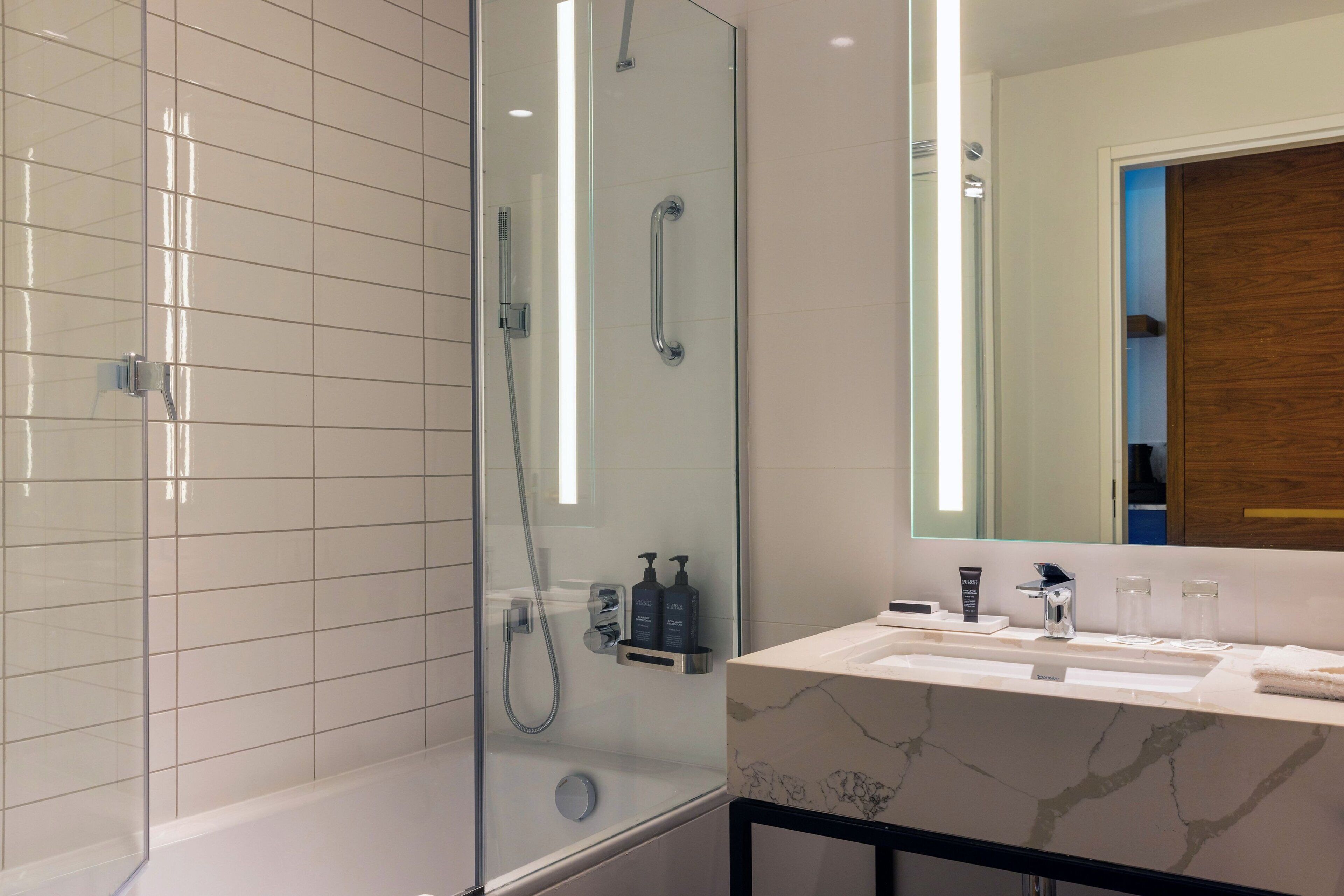 Une salle de bain moderne avec une douche à parois de verre, un lavabo en marbre et un grand miroir.