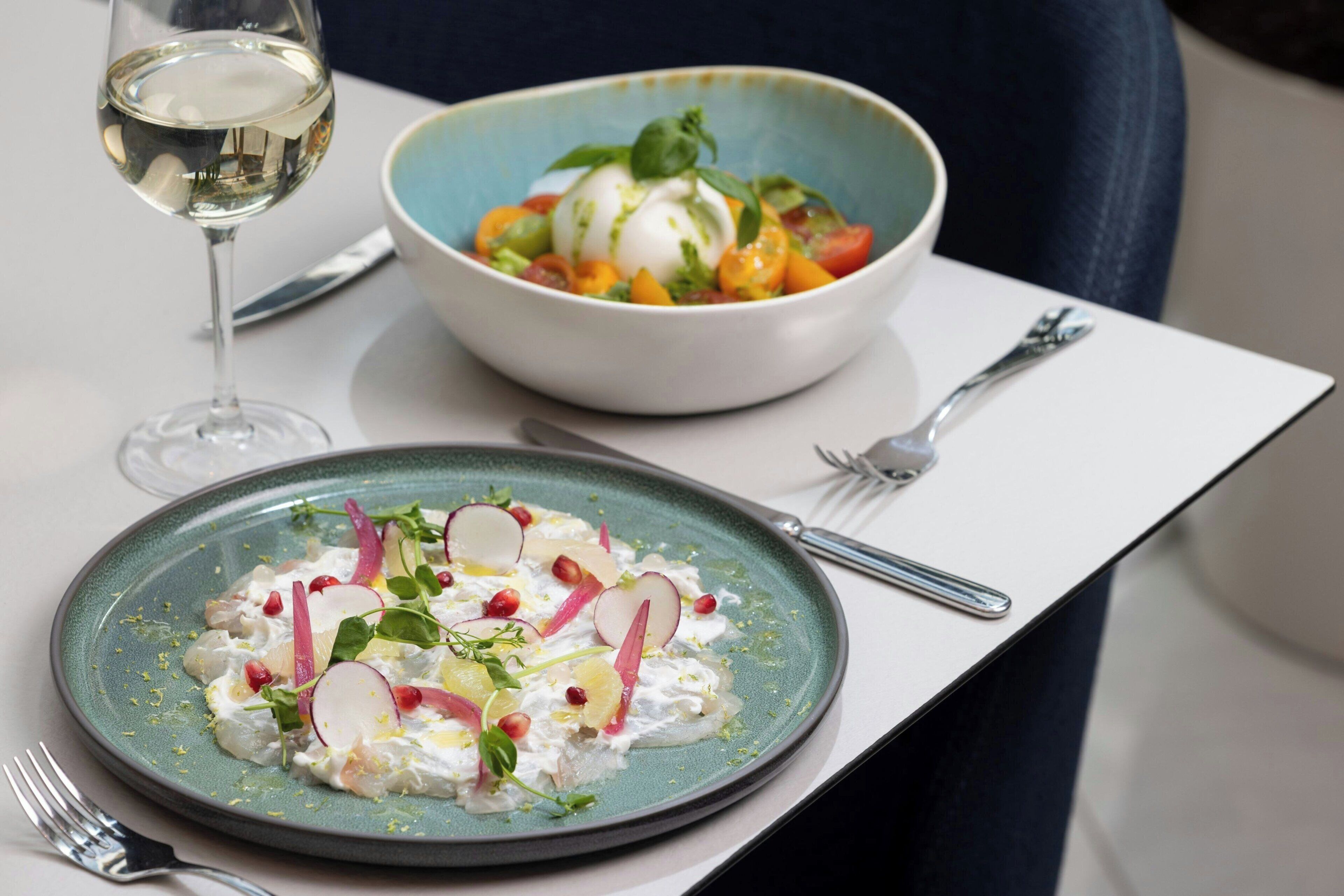 A dining table with a plate of food, a glass of white wine, and cutlery.