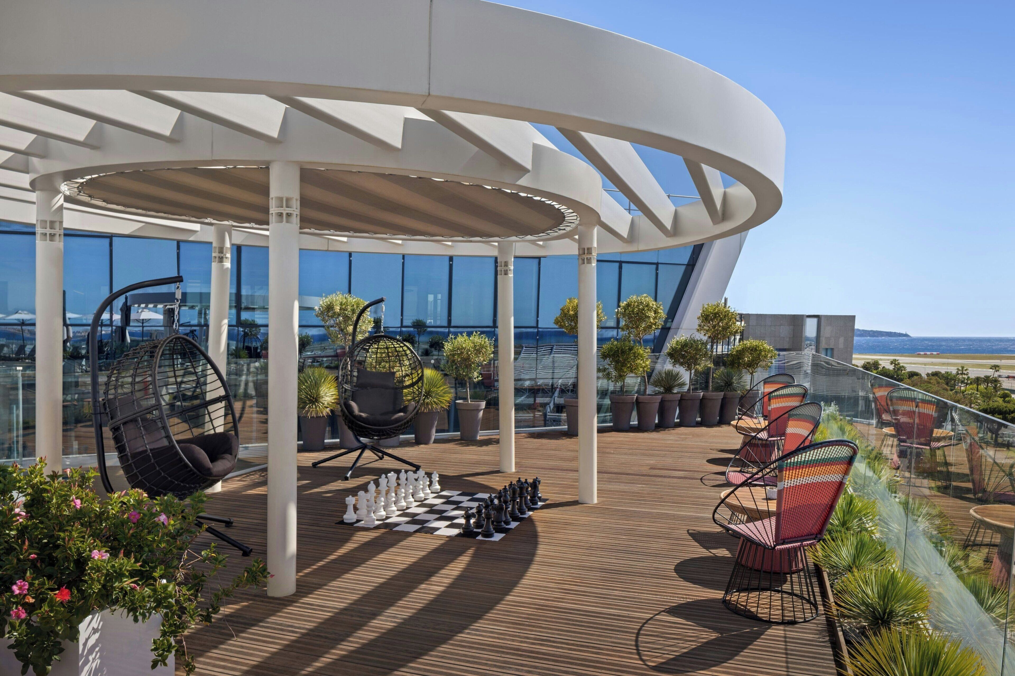 Een modern terras buiten met een schaakbordpatroon, loungesteilen en potplanten.
