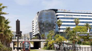 A modern hotel with a curved facade, a pedestrian bridge, and a train passing underneath.